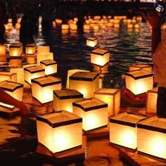 many lanterns floating in the water with people standing around them and one person holding a cell phone