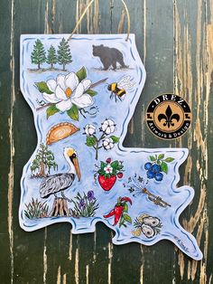 a state shaped sticker with flowers, birds and other things in it on a wooden background