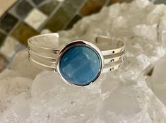 This lovely cuff bracelet is set with a spectacular Leland blue stone. The stone is 20 mm in diameter. This bracelet has a substantial silver coating that adjusts to accommodate ost wrist sizes. It does not tarnish as easily as Sterling silver does. Leland Blue is not a natural stone but rather a byproduct of smelting iron ore in the late 1800s. Blue Polished Bangle Cuff Bracelet, Elegant Blue Cuff Bracelet With Polished Finish, Blue Round Cuff Bracelet For Formal Occasions, Formal Blue Gemstone Cuff Bracelet, Blue Nickel-free Bangle Cuff Bracelet, Blue Sterling Silver Round Cuff Bracelet, Blue Cuff Bracelet Gift, Adjustable Blue Gemstone Cuff Bracelet, Leland Blue Stone