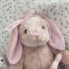 a stuffed rabbit sitting on top of a bed next to a small teddy bear with a pink bow