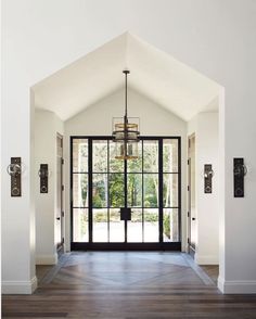 an open door leading into a large room with wooden floors and white walls, along with two chandeliers hanging from the ceiling