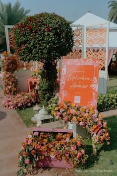 an orange sign sitting on top of a lush green field next to flowers and trees