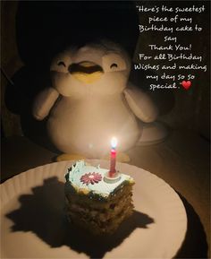 a birthday cake with a lit candle in the shape of a penguin sitting next to it