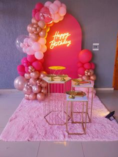 a birthday party with balloons, cake and other items on the floor in front of a neon sign