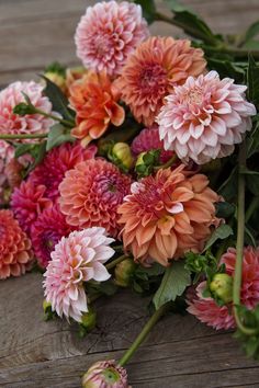 a bunch of pink and orange flowers sitting on top of a wooden table next to green leaves