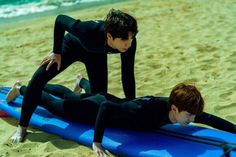 two people in wetsuits laying on surfboards on the beach