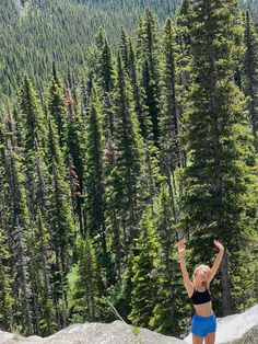 a woman is throwing a frisbee in the air near some trees and mountains