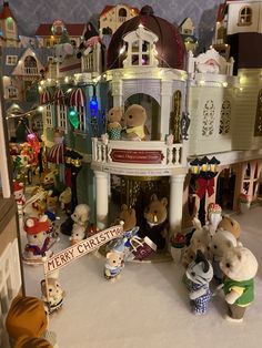 a group of teddy bears standing in front of a christmas village with lights and decorations