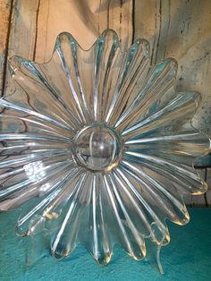 a clear glass flower dish sitting on top of a blue tablecloth covered floor next to a wooden wall