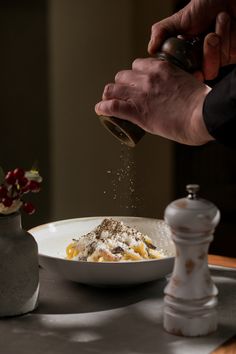 a person is sprinkling salt on food in a white bowl next to a vase