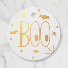 a white and gold boo halloween ornament on a marble surface with bats, spider webs and stars