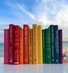 a row of colorful books sitting on top of a white table next to the ocean