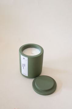 a candle sitting on top of a white table next to a green container with a label