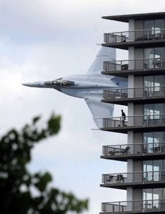 a fighter jet flying past a tall building with balconies on it's sides