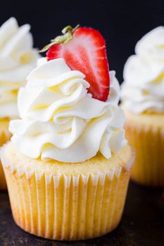 three cupcakes with white frosting and a strawberry sitting on top of them