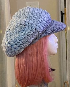 a mannequin head wearing a knitted hat with pink and blue hair in front of a door