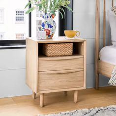 a bedroom with a bed, nightstand and vase on the end table in front of a window