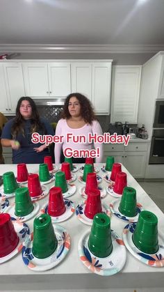 two women standing in front of a table with cups and saucers on it that says super fun holiday game