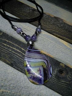 This listing is for a purple and yellow banded agate necklace. The drop pendant is about 2 inches long.   The pendant is hung on a rat tail cord with accent beads of amethyst and metal.  Slip knots allow the necklace to be fitted to your tastes.     All of our pendulums, rosaries, prayer chains, and jewelry come to you in a lovely presentation bag. We, at The Broken Vial, want to tell you that all items are sold for entertainment, and as curio, only, and that we do not guarantee that any item wi Purple Gemstone Amulet Necklace, Artisan Purple Adjustable Necklace, Purple Spiritual Necklace With Large Pendant, Spiritual Purple Necklace With Large Pendant, Spiritual Purple Pendant Necklace, Unique Adjustable Purple Necklace, Handmade Purple Agate Beaded Necklaces, Multicolor Adjustable Amethyst Necklace, Adjustable Agate Amulet Necklace