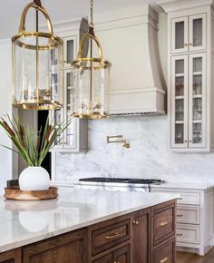 a kitchen with marble counter tops and gold accents on the lights hanging from the ceiling