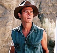 a man in a cowboy hat standing next to a surfboard