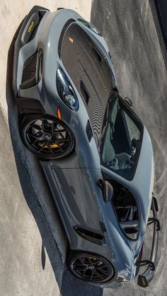 the top view of a grey sports car parked in a parking lot next to a cement wall