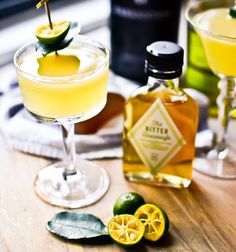 two glasses filled with drinks sitting on top of a wooden table next to lemons