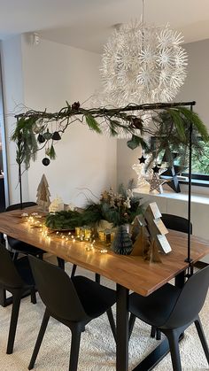 a dining room table decorated for christmas with greenery and lights on the top, surrounded by black chairs