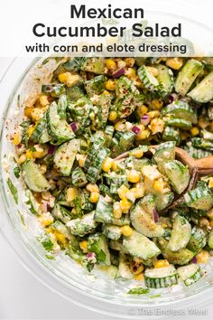 a glass bowl filled with cucumber and corn salad next to a wooden spoon