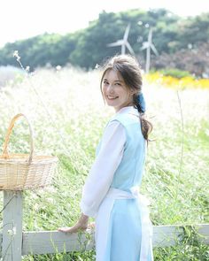 a woman in a blue dress standing next to a wooden fence with a basket on it