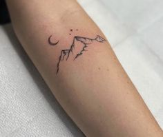 a small tattoo on the arm of a woman with mountains and stars in the sky