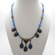 "Vintage Art Deco Blue Glass Necklace with Cabochon Fringe Center Drops Pretty 17\" White Metal and Blue Glass Fringe Necklace. It has fourteen 6.8mm faceted stepped topped art deco beads spaced between 12.7mm x 6.6mm dotted links. To top it off, it has five oval cabochon (7.4mm x 5.25mm) blue glass stones in a fringe pattern that hangs app. 1 1/2\". The blue is very similar to blue chalcedony in an aquamarine opaque color. Item #: NVCJ108 Style: Art Deco Metal: White Base Metal Condition: Very Blue Vintage Cabochon Jewelry, Vintage Blue Cabochon Jewelry, Blue Metal Jewelry With Faceted Beads, Formal Blue Cabochon Necklace, Blue Art Deco Necklace For Formal Occasions, Vintage Blue Necklaces With Polished Beads, Vintage Blue Czech Glass Necklace, Vintage Adjustable Blue Necklace, Blue Art Deco Jewelry For Jewelry Making