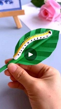 a person holding a paper leaf with a caterpillar on it's side