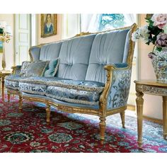 a blue couch sitting on top of a red rug next to a vase filled with flowers