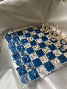 a blue and white chess board with gold pieces on it, sitting on a white cloth