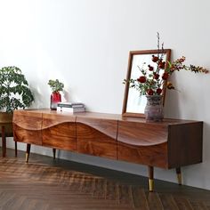 a wooden table with a mirror on top of it next to two plants and a potted plant