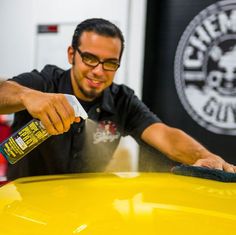 a man sanding the hood of a yellow car with a sponge and a cloth