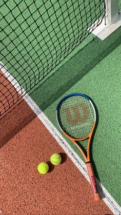 two tennis balls and a racket on the ground in front of a green net