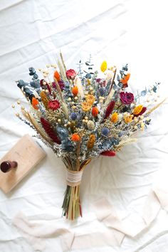 a bouquet of dried flowers sitting on top of a white sheet next to a piece of wood