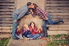 a man and woman kissing while sitting on the ground with their children in front of them