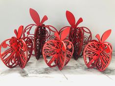 four red paper cut apples sitting next to each other on a marble counter top with white walls in the background