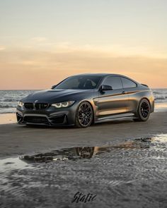 a grey car parked on top of a sandy beach next to the ocean at sunset