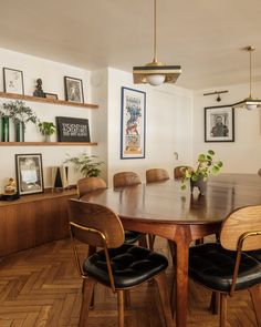 a dining room table with black chairs and pictures on the wall above it, along with wooden shelves