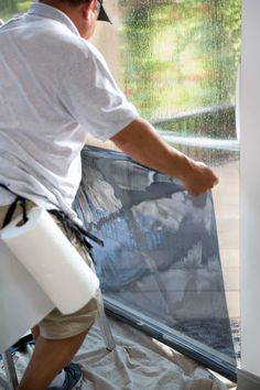 a man in white shirt and khaki shorts working on an outdoor screen door