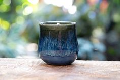 a blue and black cup sitting on top of a wooden table next to some trees