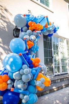 blue and orange balloons are hanging from the side of a building in front of a house