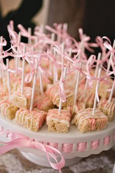 cake pops with pink icing and bows on a white platter at a wedding reception