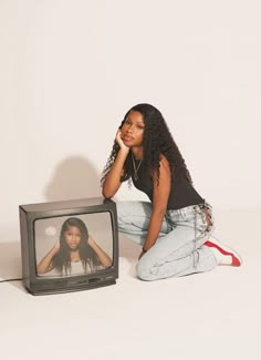 a woman sitting on the ground next to a tv with an image of herself on it