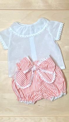 This unique set is perfect for your stylish fashionista! The short-sleeved blouse is made from white Swiss dotted plumeti cotton with a round ruffled collar and intricate crochet lace trimmings. Paired with coral and white striped bubble shorts, featuring a large bow and delicate lace details. A must-have for any fashion-forward baby or toddler girl!Product Details: Cotton 100% Crochet cotton lace Nacar (mother of pearl-shell) button French seam Very limited Cute Ruffled Short Sleeve Sets, White Short Sleeve Sets For Spring, White Short Sleeve Spring Sets, Cotton Polka Dot Sets For Summer, White Ruffled Summer Sets, Polka Dot Cotton Sets For Spring, Spring Cotton Sets With Polka Dot, Spring Cotton Polka Dot Sets, Cute Polka Dot Cotton Set