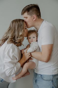 a man and woman holding a baby in their arms while they are kissing each other